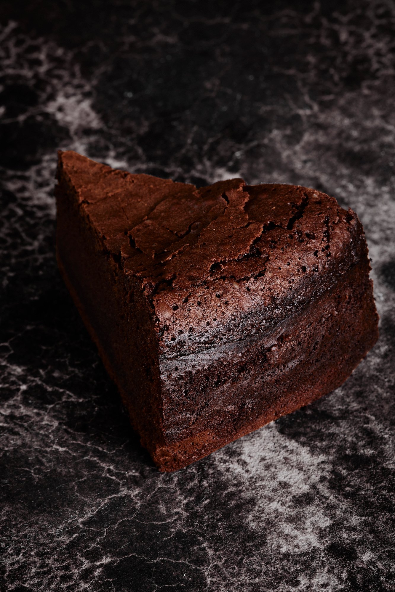 A single wedge of flourless chocolate cake on dark marble, Chocolate by Hannah Caldwell