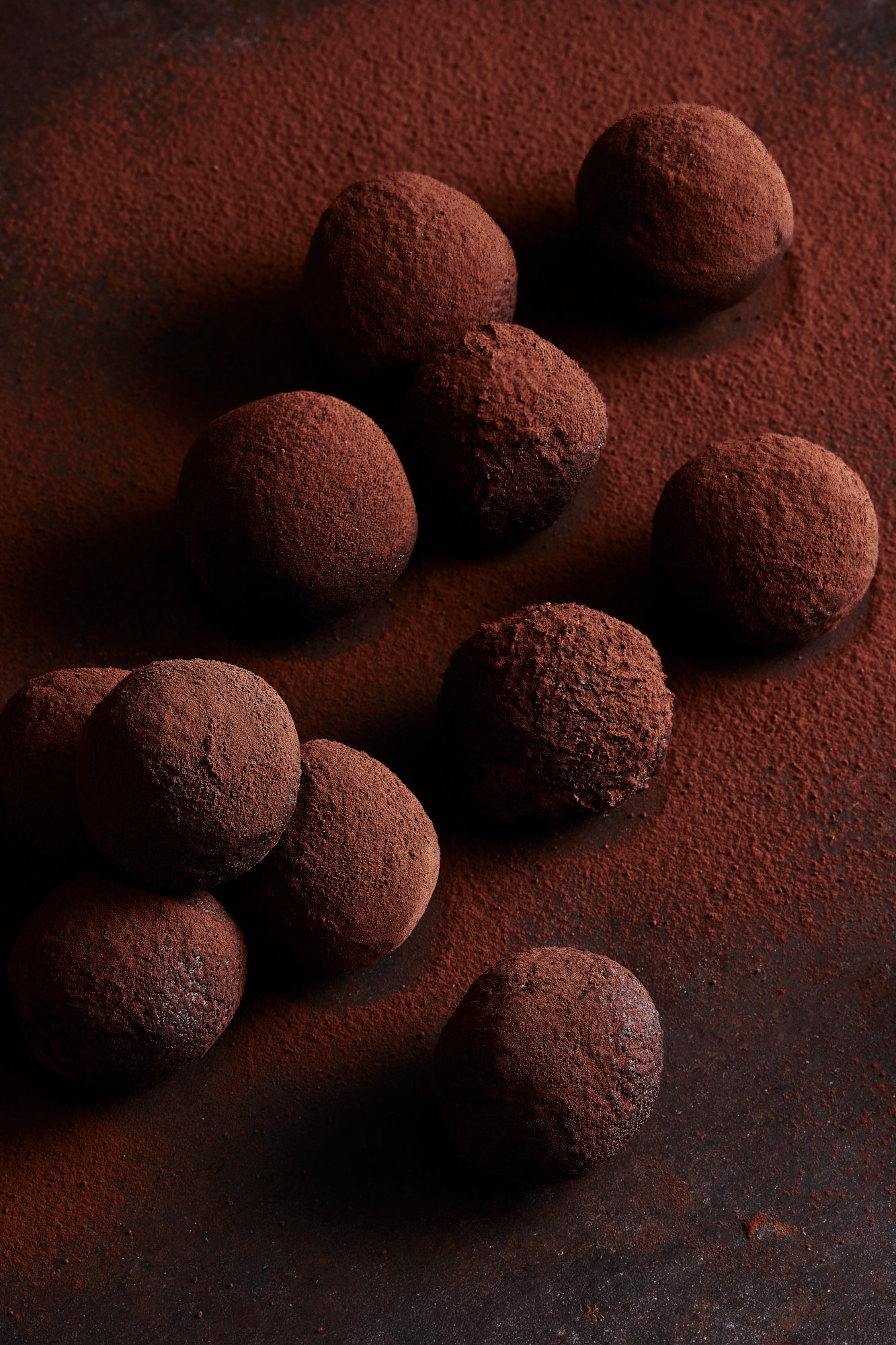 Dusted chocolate truffles set in a diagonal line across dark cocoa powder, Chocolate by Hannah Caldwell