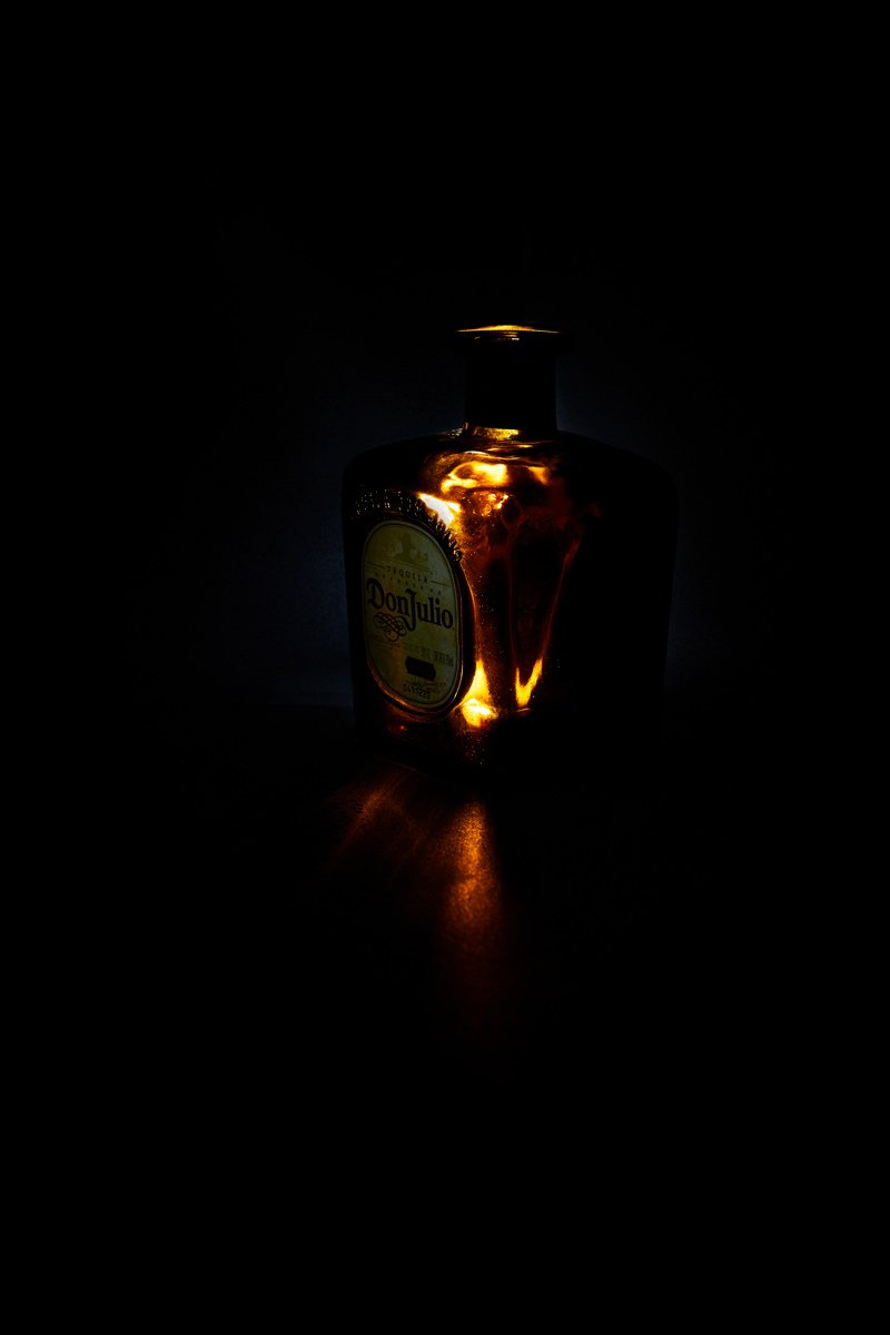 An amber spirit bottle burning warm in the dark, from Glass by Hannah Caldwell