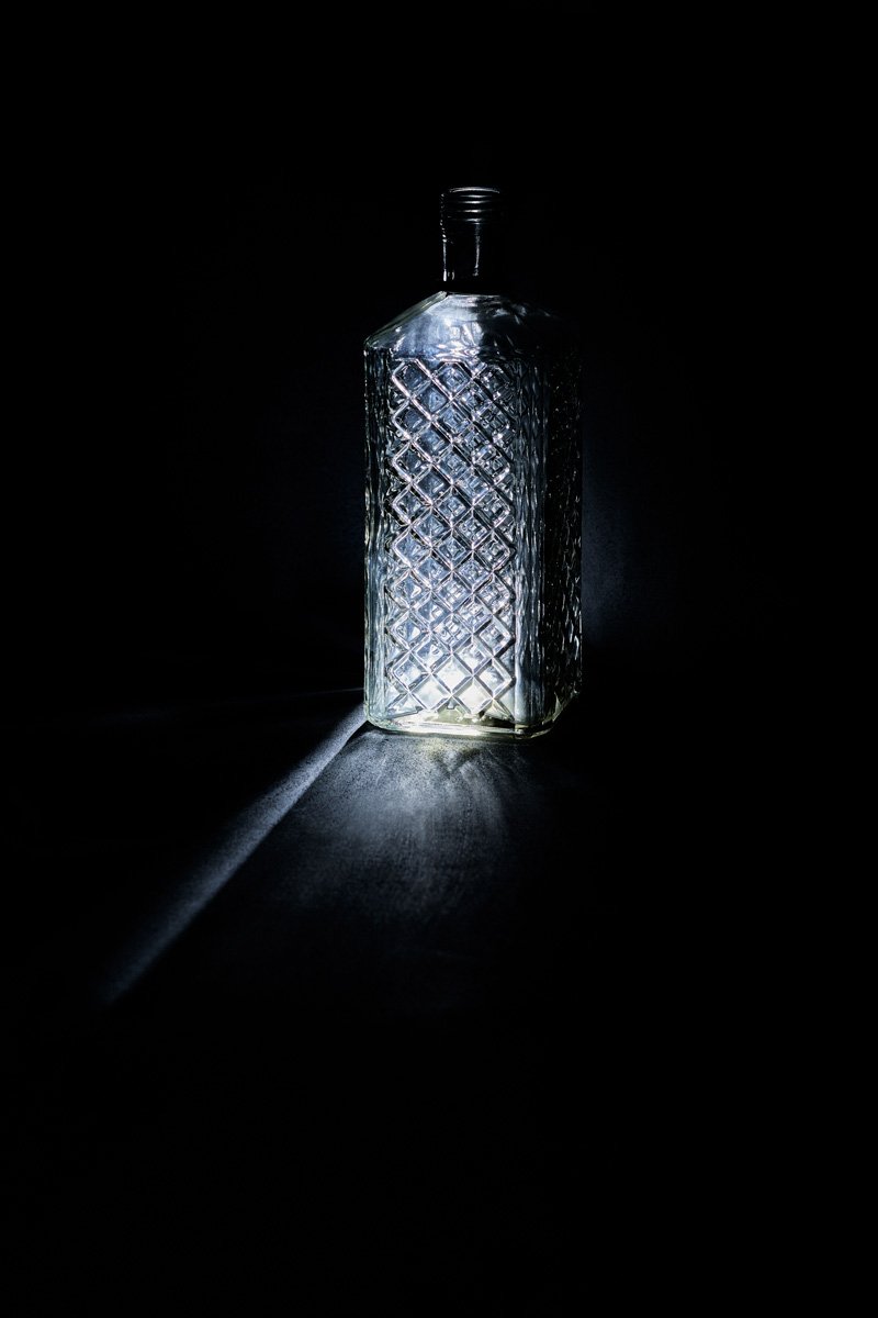 A diamond cut bottle throwing a bright caustic pool toward the viewer, Glass by Hannah Caldwell
