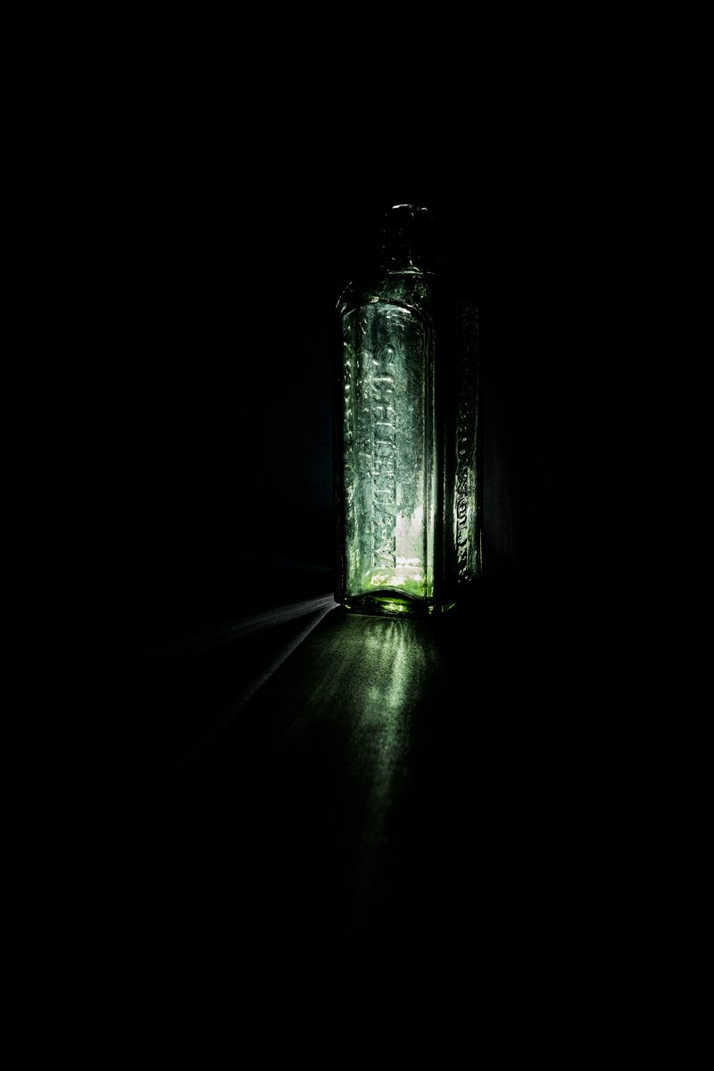 A green apothecary bottle spilling a pool of green light, Glass by Hannah Caldwell