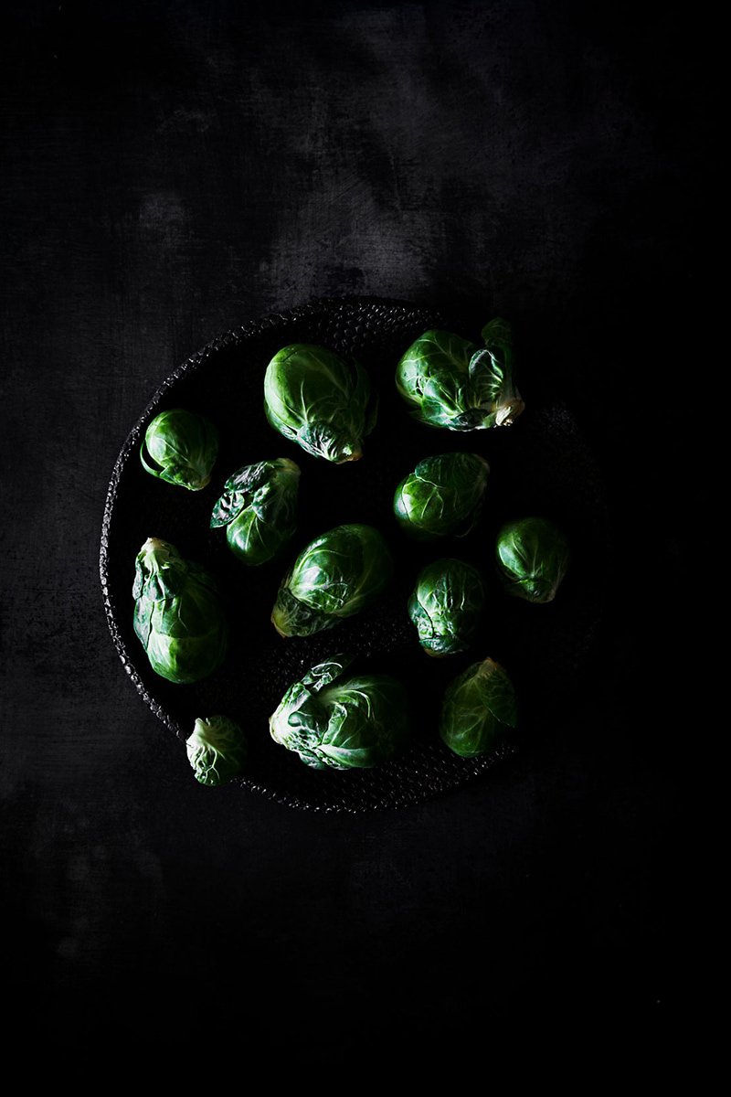 Brussels sprouts gathered in a dark bowl, RAW by Hannah Caldwell