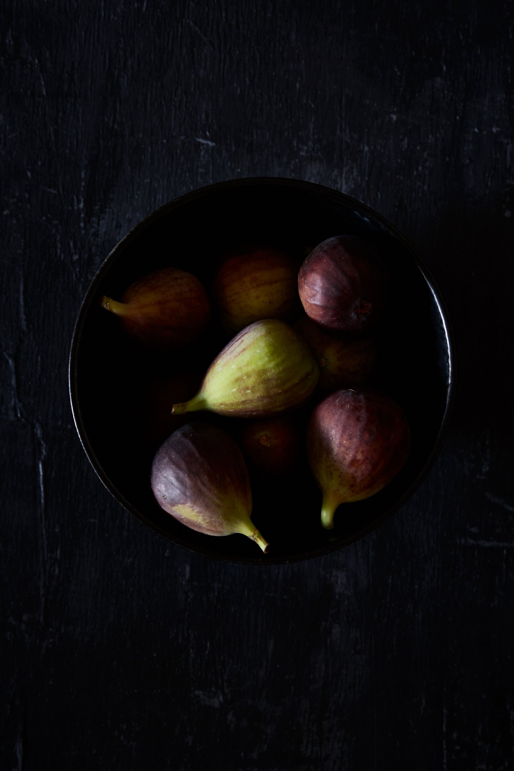 Fresh figs piled in a dark bowl, RAW by Hannah Caldwell