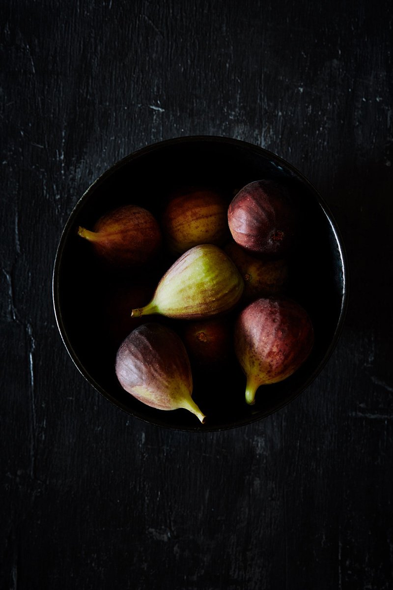 Fresh figs piled in a dark bowl, RAW by Hannah Caldwell
