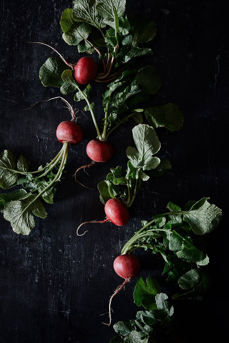 Radishes with their leaves on a dark board, RAW by Hannah Caldwell