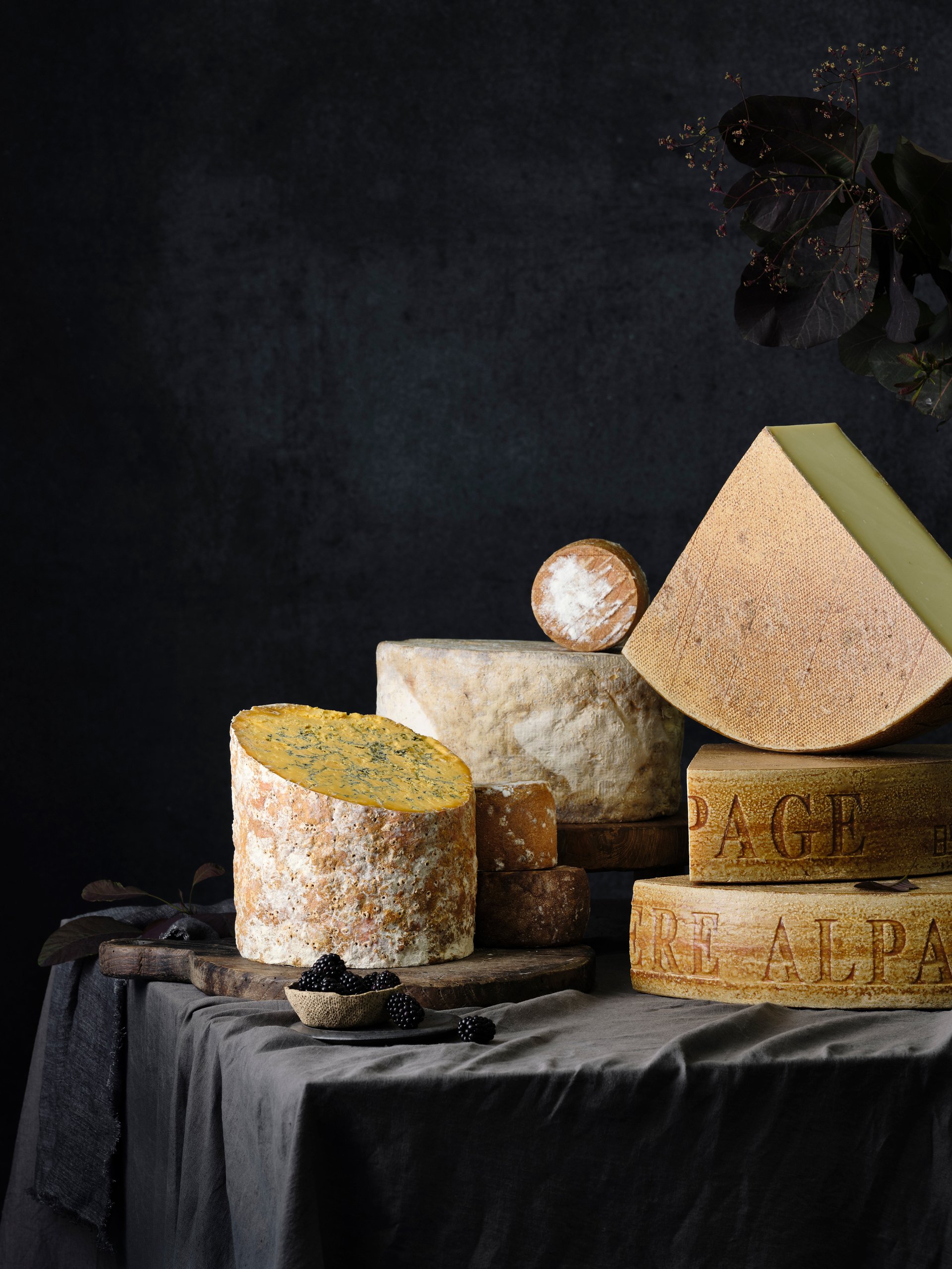 A stack and arrangement of many cheese wheels and wedges on wooden boards, Savour and Grace by Hannah Caldwell