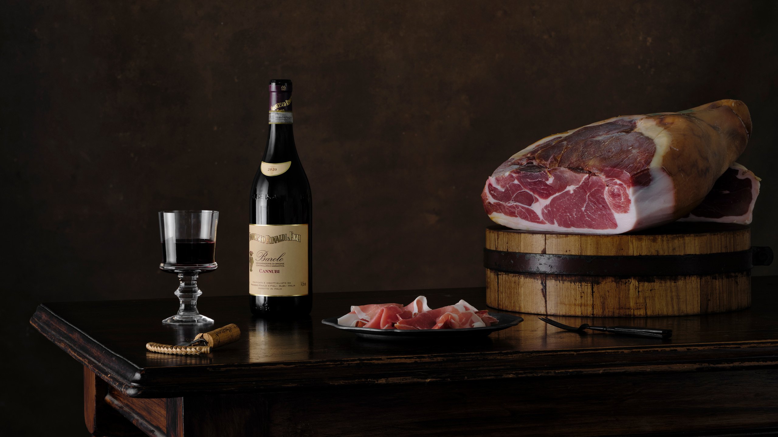 A whole prosciutto leg on a barrel with a bottle of wine and a plate of sliced prosciutto, Savour and Grace by Hannah Caldwell